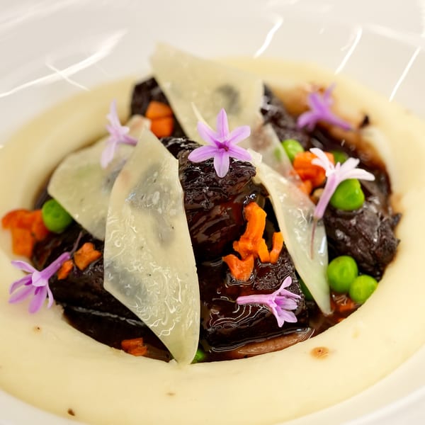Braised short ribs with parmesan, peas, carrots, and edible flowers on a bed of mashed potatoes.