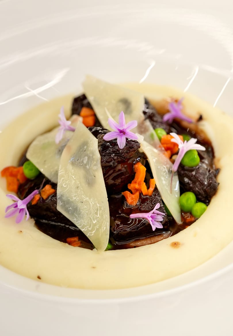 Braised short ribs with parmesan, peas, carrots, and edible flowers on a bed of mashed potatoes.