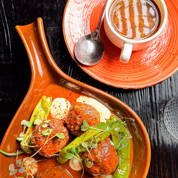 Meatballs in red sauce with green peppers and microgreens, alongside a cup of soup.