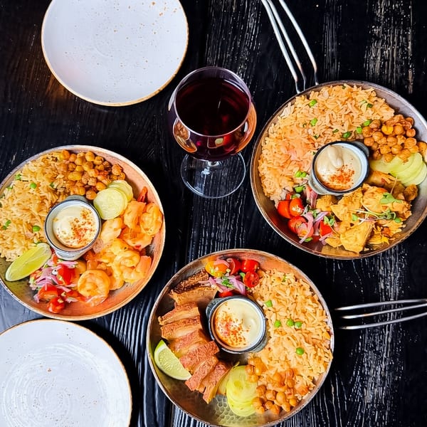 Three pans of rice dishes with shrimp, pork, and chicken, with a glass of red wine.