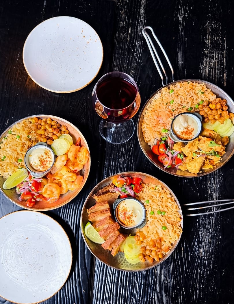 Three pans of rice dishes with shrimp, pork, and chicken, with a glass of red wine.