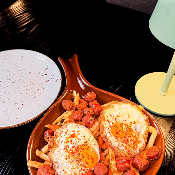 A brown dish filled with french fries, sliced sausage, and two fried eggs with paprika.