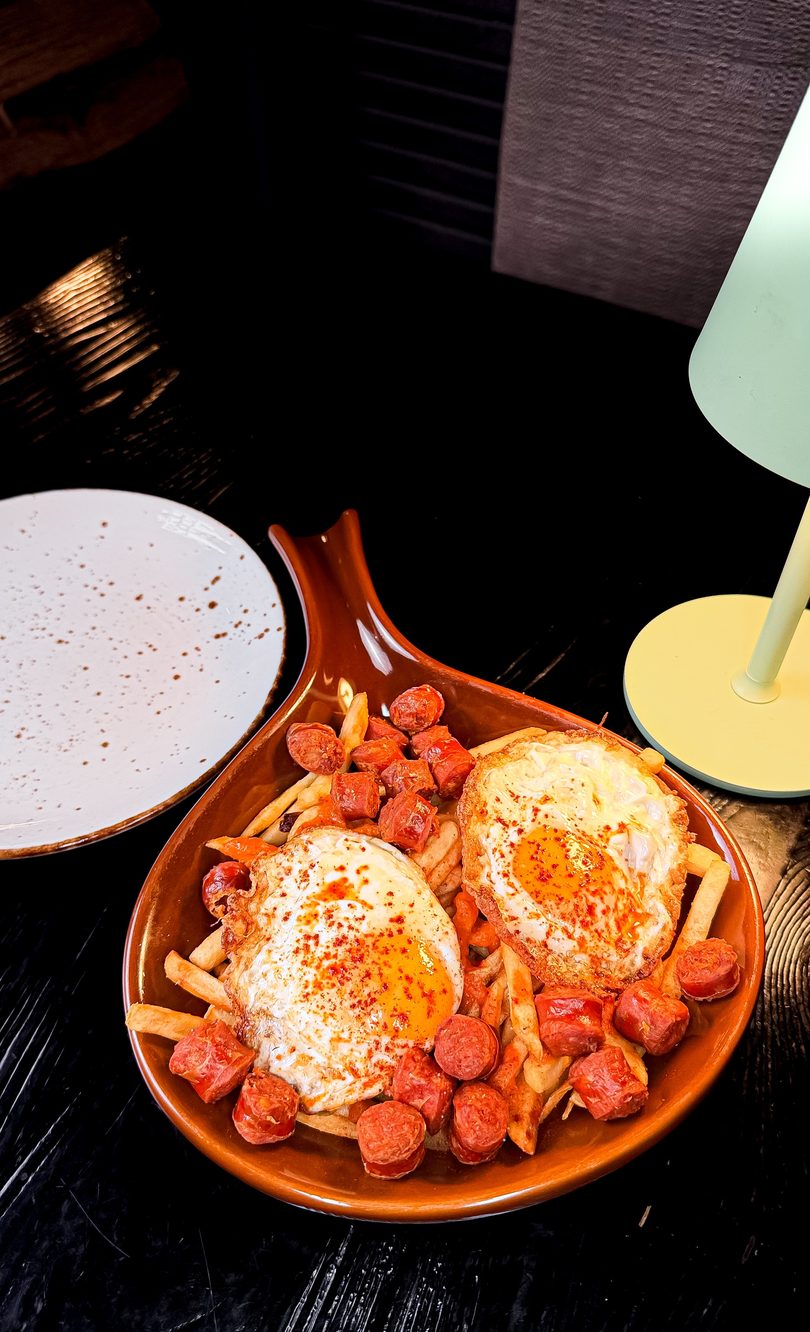 A brown dish filled with french fries, sliced sausage, and two fried eggs with paprika.