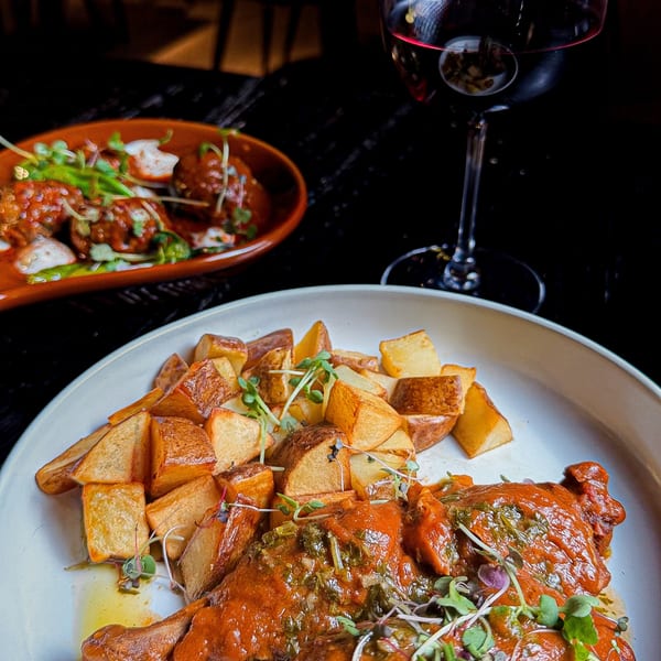 Braised meat with roasted potatoes and a glass of red wine on a dark table.